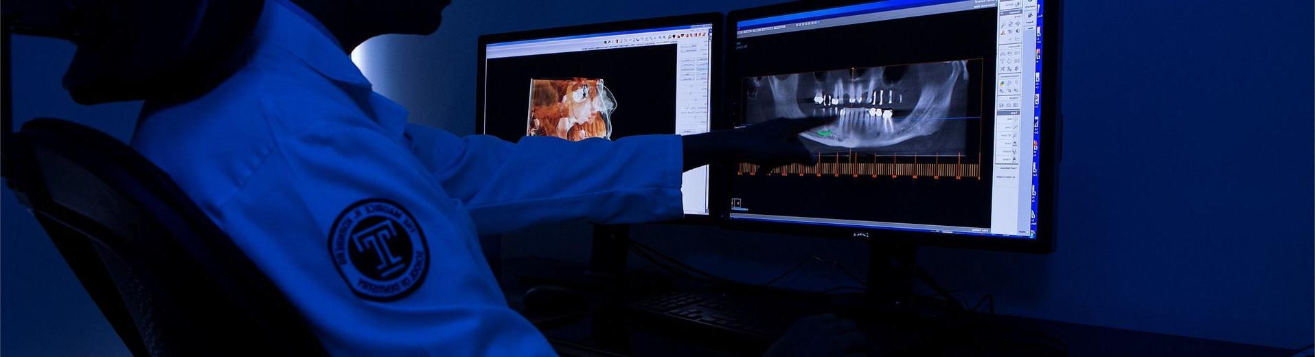 A male dental student looking at dental X-rays on a computer screen.