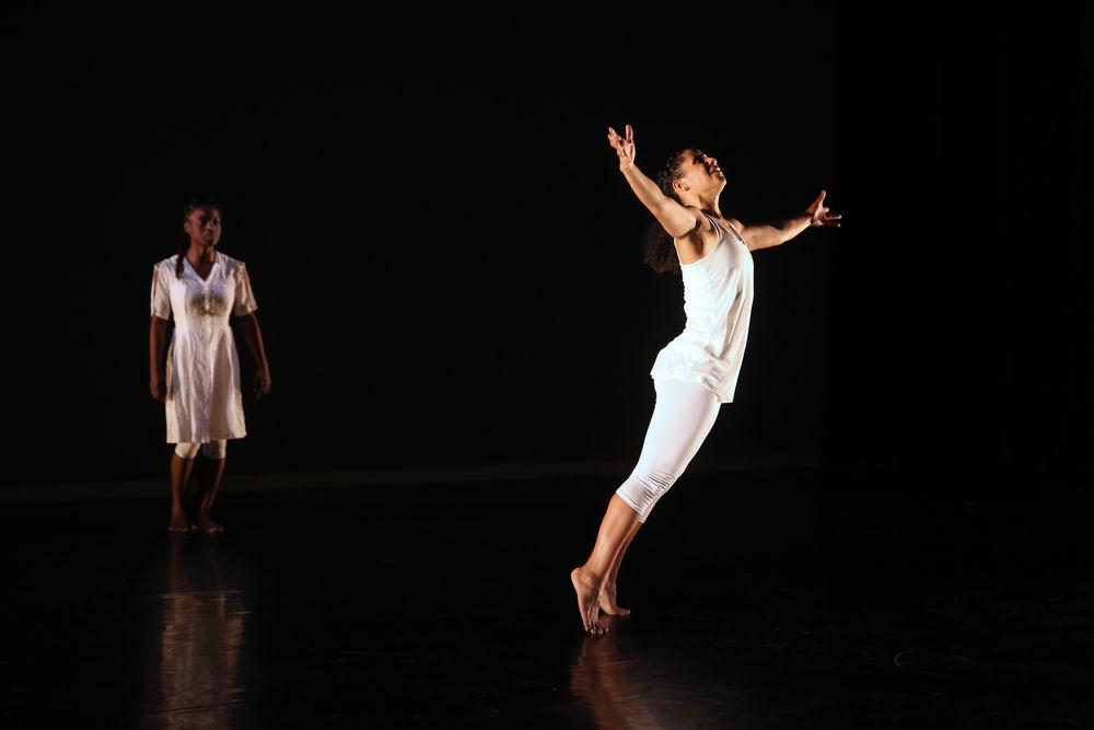 A dancer leaps on stage, with another standing behind her. 